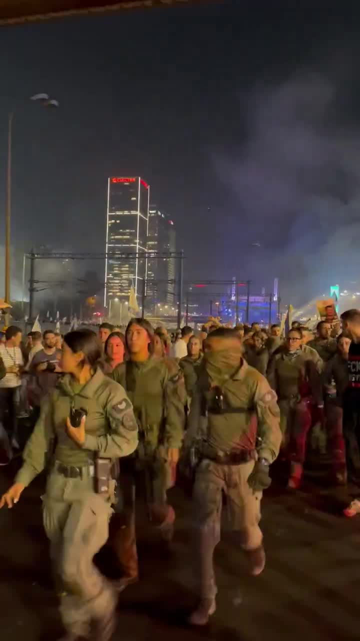 Polizisten in Ayalon South rücken in einer großen Gruppe aus, um Brände mit Feuerlöschern zu löschen, Hunderte von Demonstranten hinter ihnen