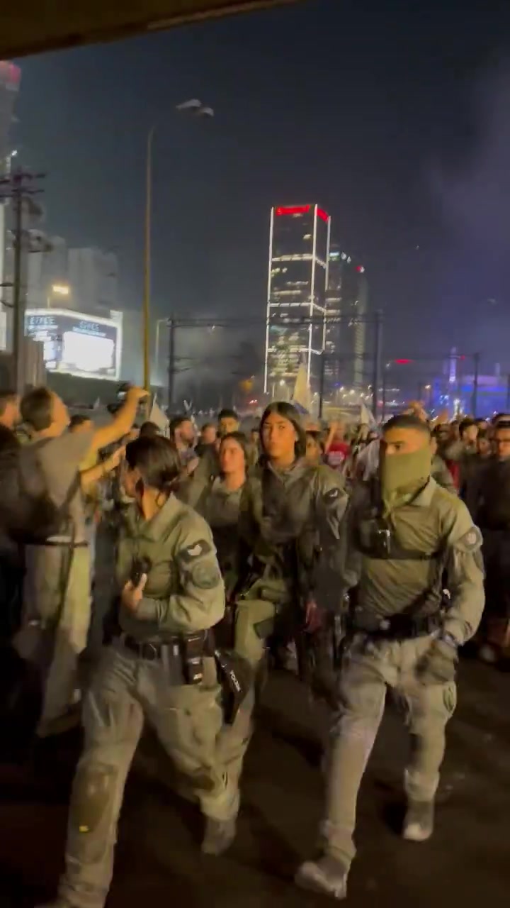 Policiais em Ayalon Sul se movem em um grande grupo para apagar incêndios com extintores de incêndio, centenas de manifestantes atrás deles