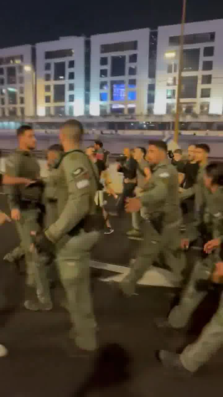 Polizisten in Ayalon South rücken in einer großen Gruppe aus, um Brände mit Feuerlöschern zu löschen, Hunderte von Demonstranten hinter ihnen