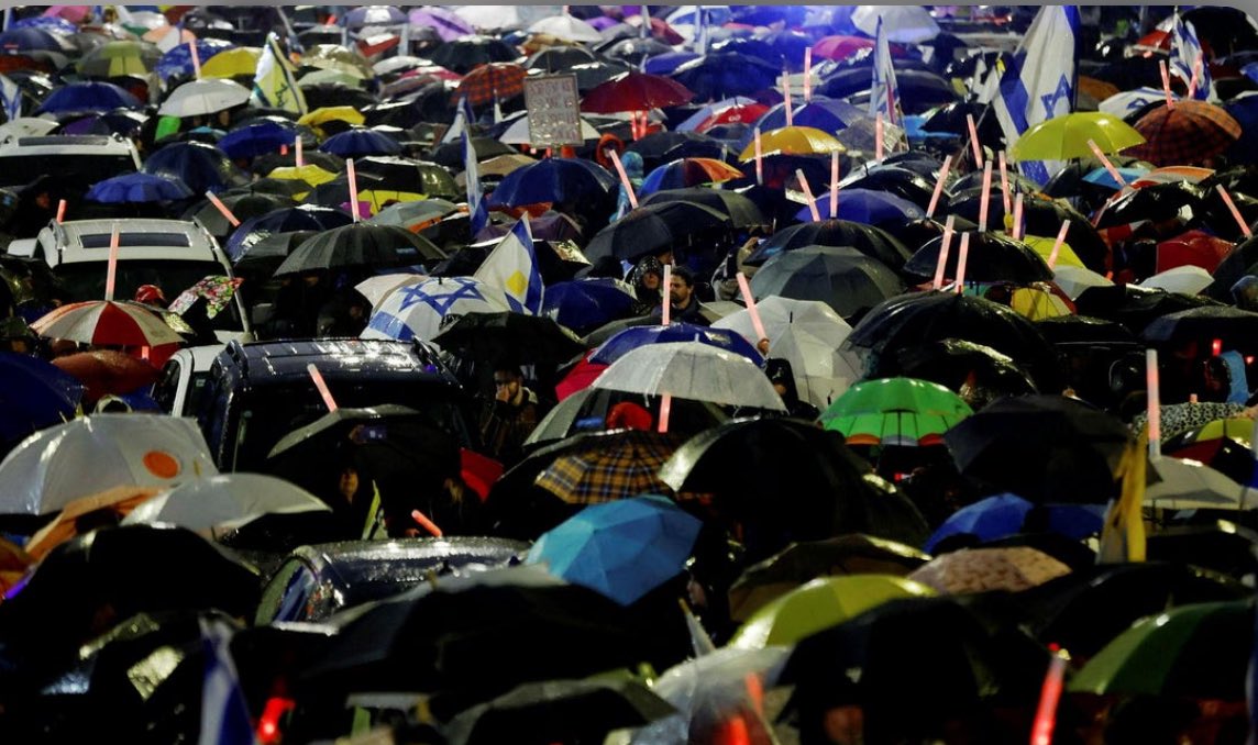 BoomUnder the driving rain, thousands hold vigil outside the cabinet room where ministers will vote to fire Shin Bet director Ronen Bar. Predecessor Carmi Gillon tells the crowd: this may be one of the last democratic protests in Israel